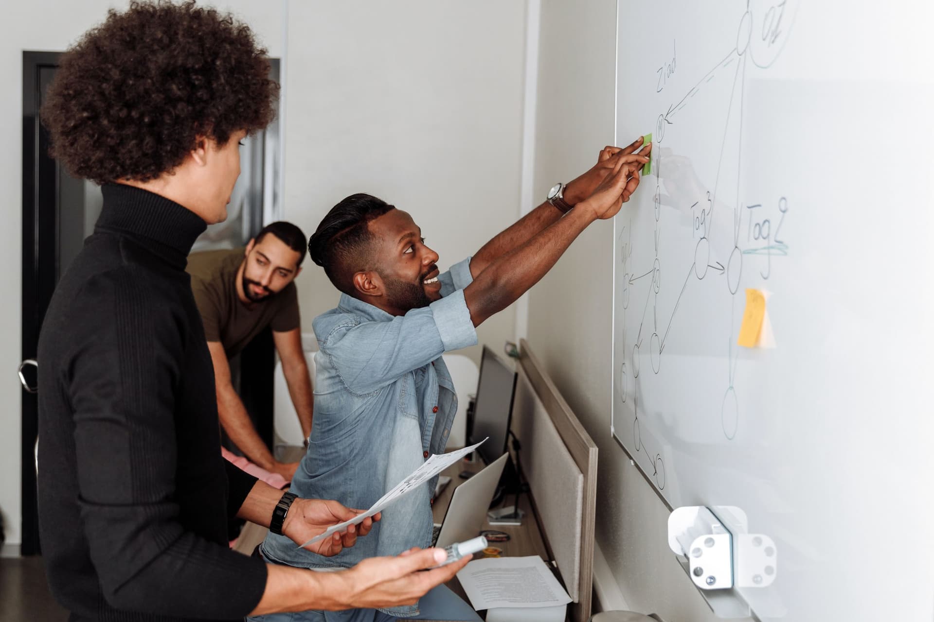 Three colleagues at a whiteboard drawing a workflow diagram of connected steps